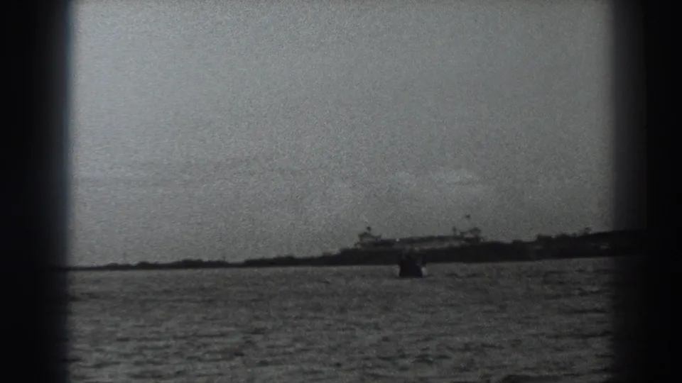 1938 8mm coastal frame near Fort Ross with a distant ship along the horizon and a small dark object in the water.