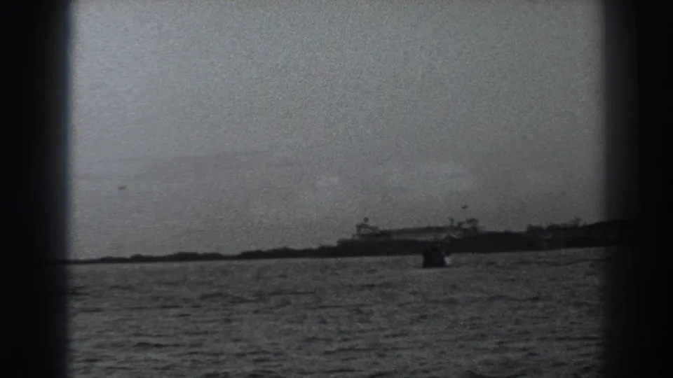 1938 Fort Ross-area shoreline seen from across the water, with distant structures and dark film edges.