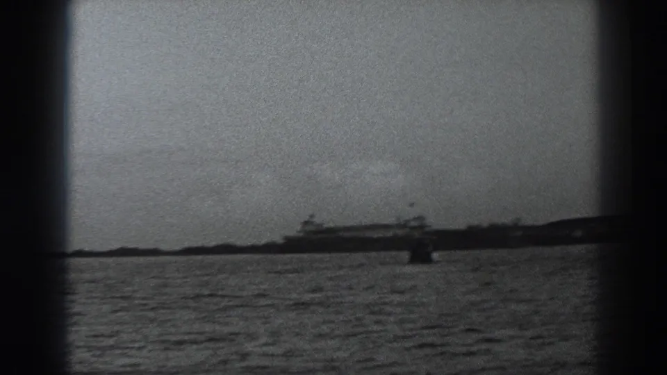 Soft 1938 home-movie frame of the Fort Ross-area shoreline, with water in the foreground and distant structures near the horizon.