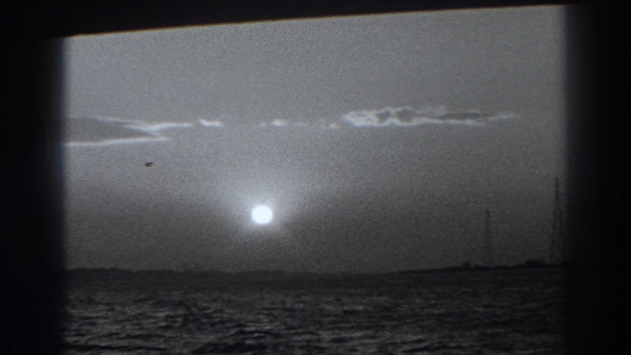 1938 Fort Ross-area home-movie frame showing the low sun above choppy coastal water and a silhouetted shoreline.