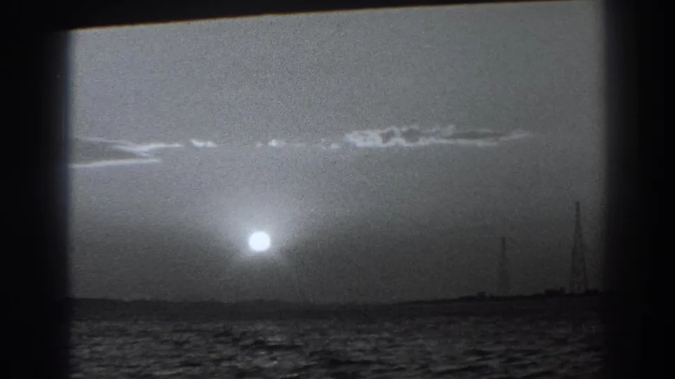 1938 coastal home-movie frame showing the sun over the ocean and distant shoreline structures near Fort Ross, California.