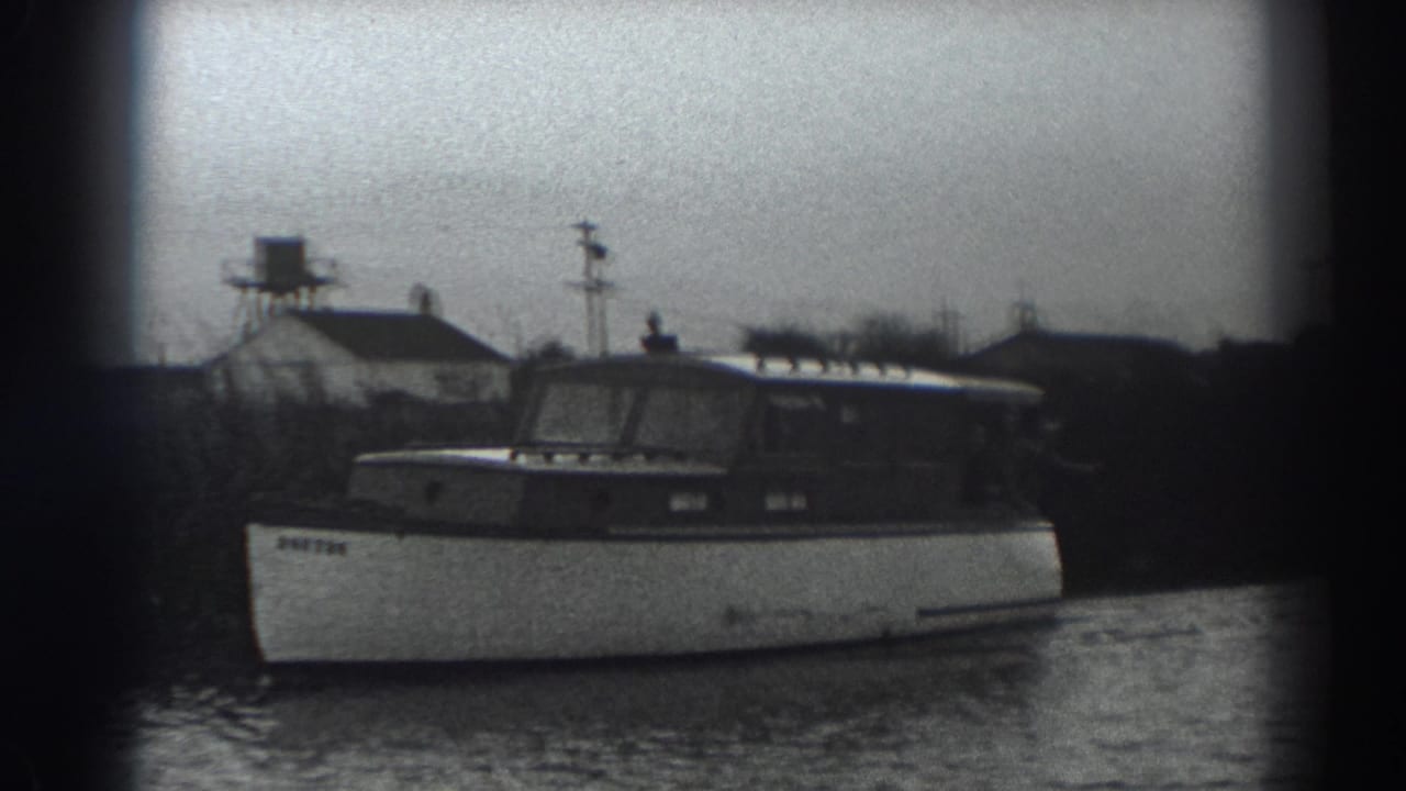 Motorboat passing along a calm river with shoreline buildings behind it.