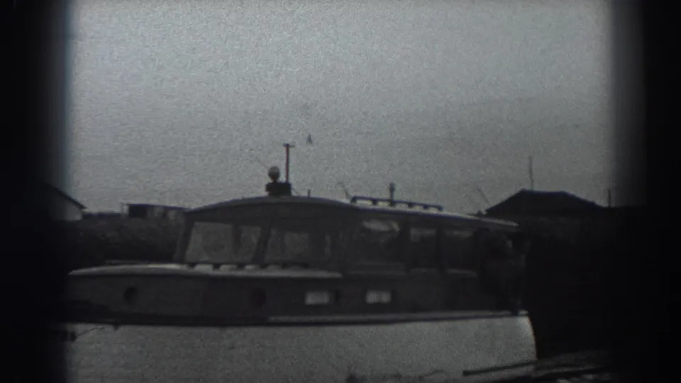 A closer 1938 Fort Ross frame shows the cabin motorboat near shore, with simple buildings, poles, and reeds in soft focus.