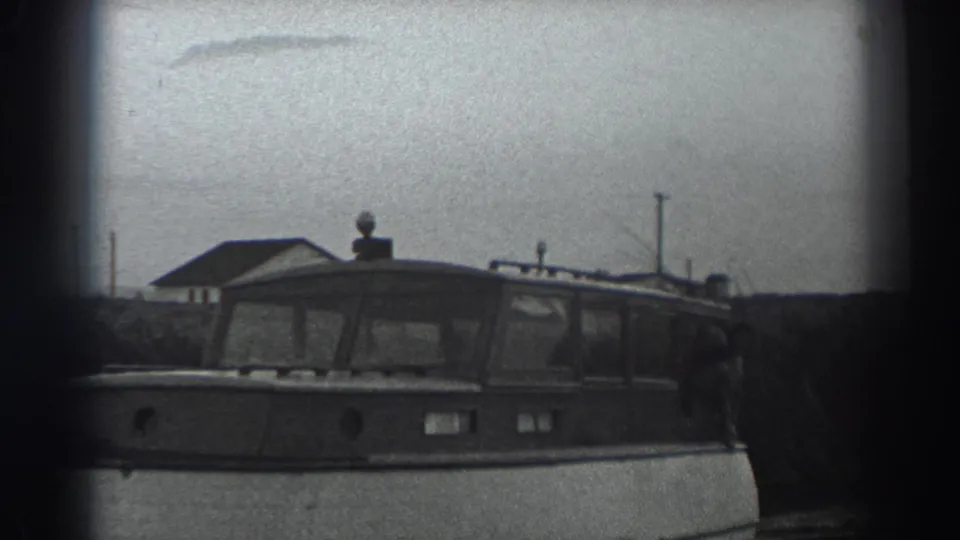 1938 Fort Ross home-movie frame showing a cabin motorboat with a white hull and dark windows on calm water.