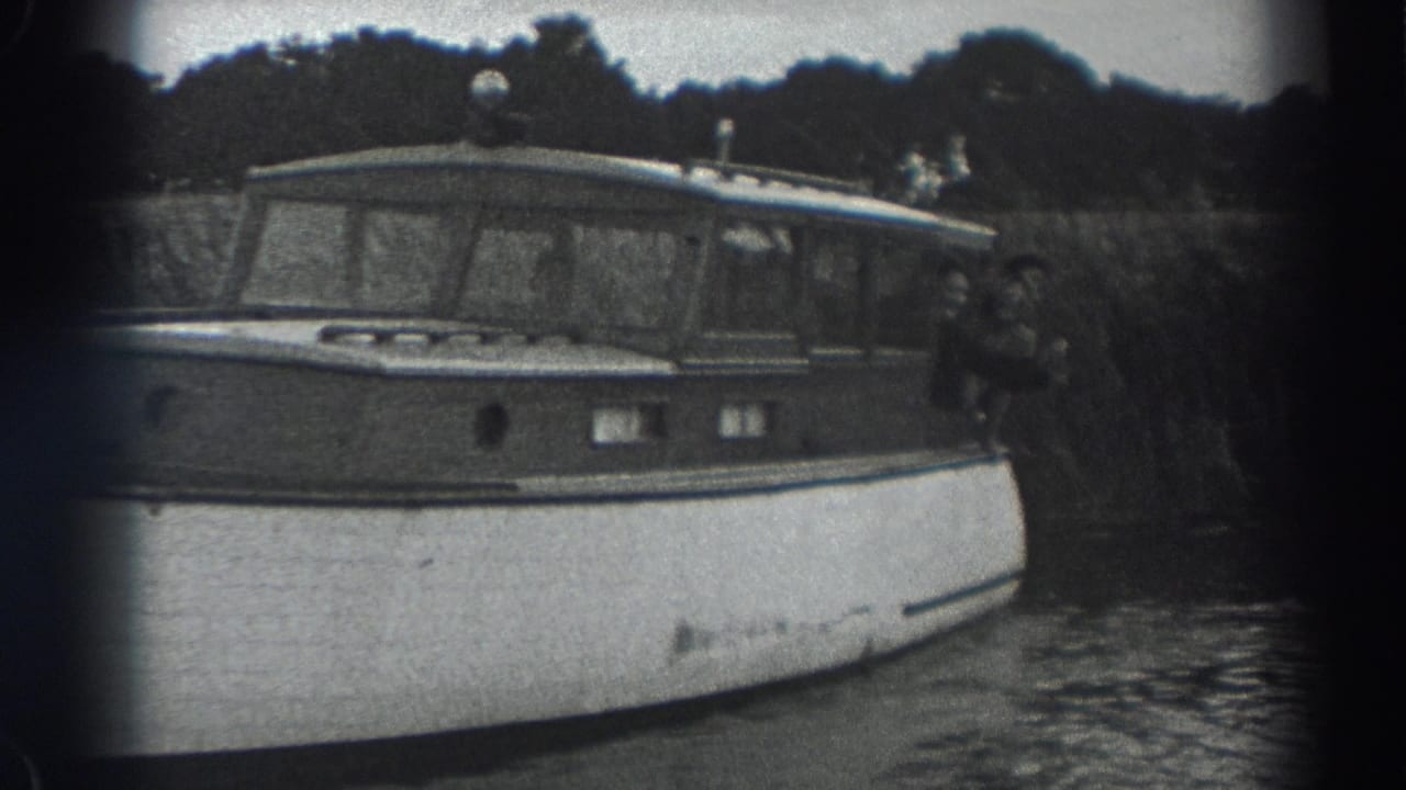 Black-and-white 1938 Fort Ross home-movie frame showing a wooden cabin motorboat on calm water with people near the stern.