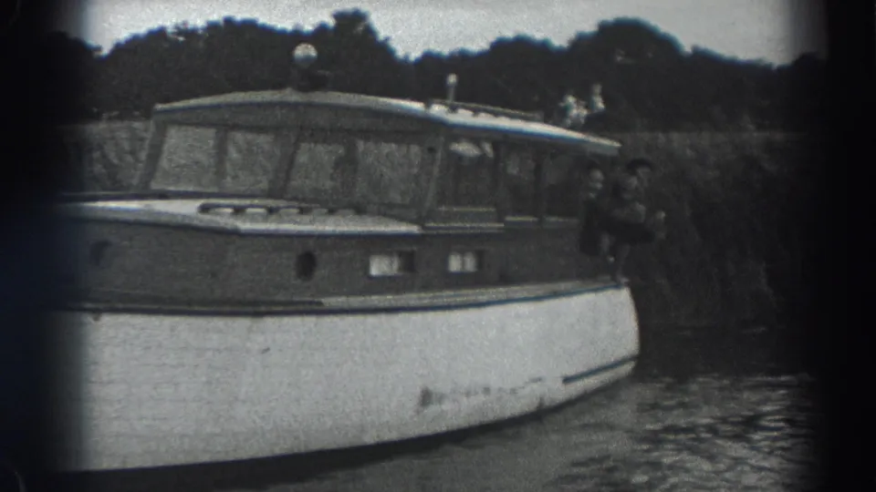 Black-and-white 1938 Fort Ross home-movie frame showing a wooden cabin motorboat on calm water with people near the stern.