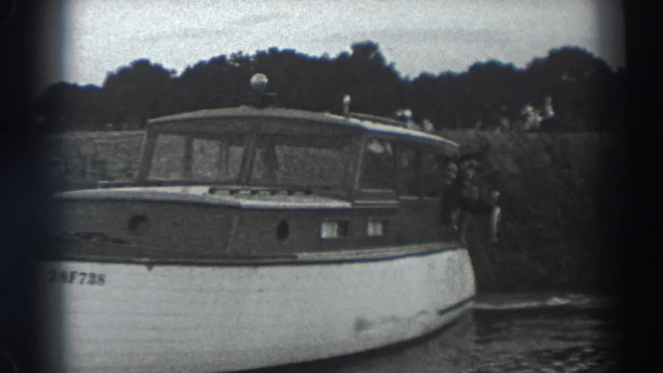 Black-and-white 1938 Fort Ross frame of the motorboat from the side, showing cabin windows, calm water, and partial hull markings.