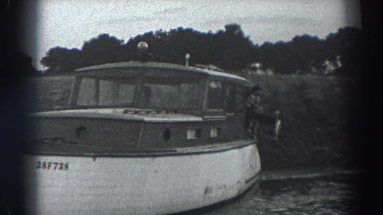 1938 Fort Ross home-movie frame showing a small cabin motorboat on calm water with a person at the stern holding a fish.