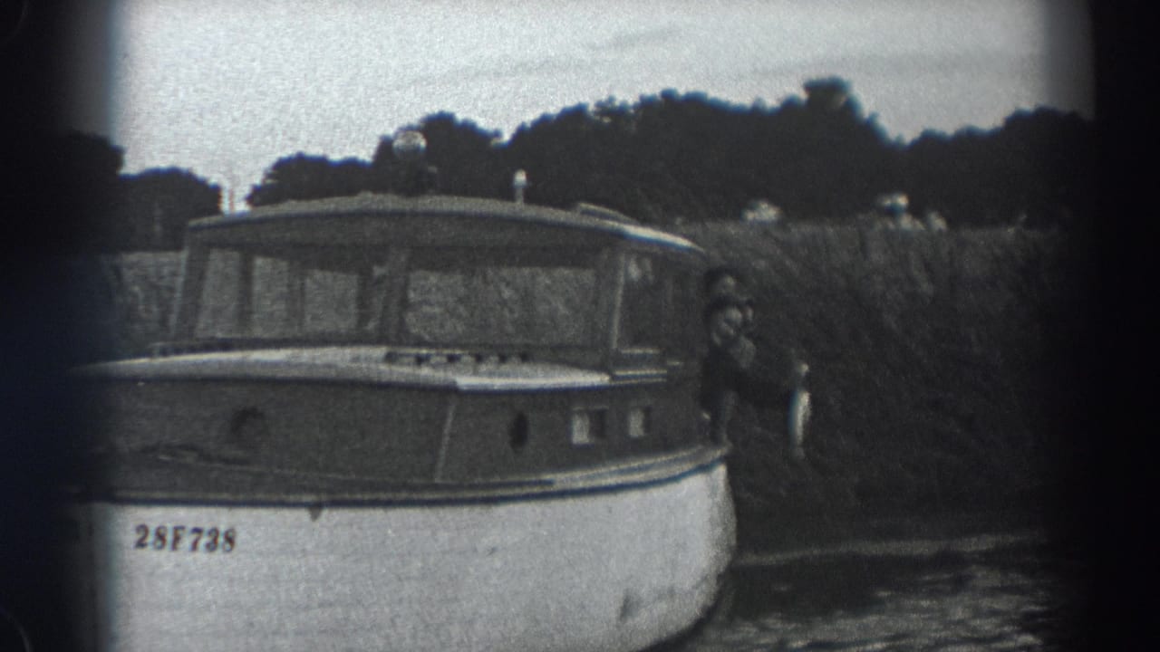 Cabin motorboat moving past reeds with a person at the stern holding a fish.