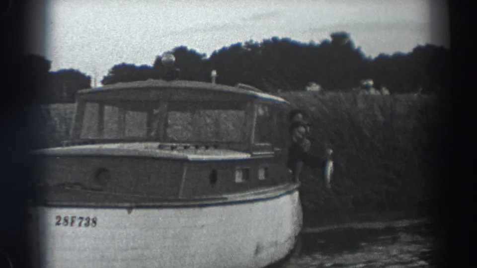 Fort Ross, California 1938 frame of a small motorboat beside reeds, with a visible person displaying a fish at the stern.