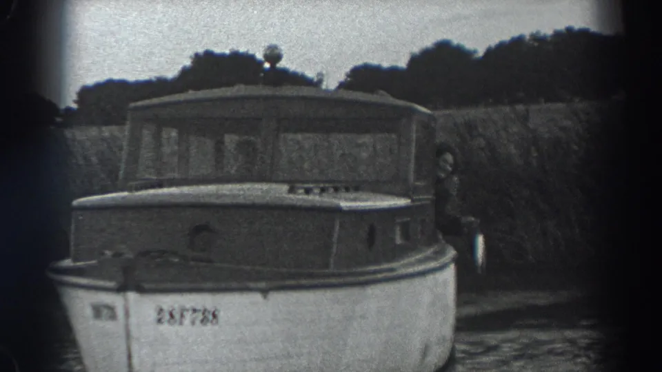 1938 Fort Ross frame showing the numbered bow of a small cabin motorboat with a person standing near the stern by the riverbank.