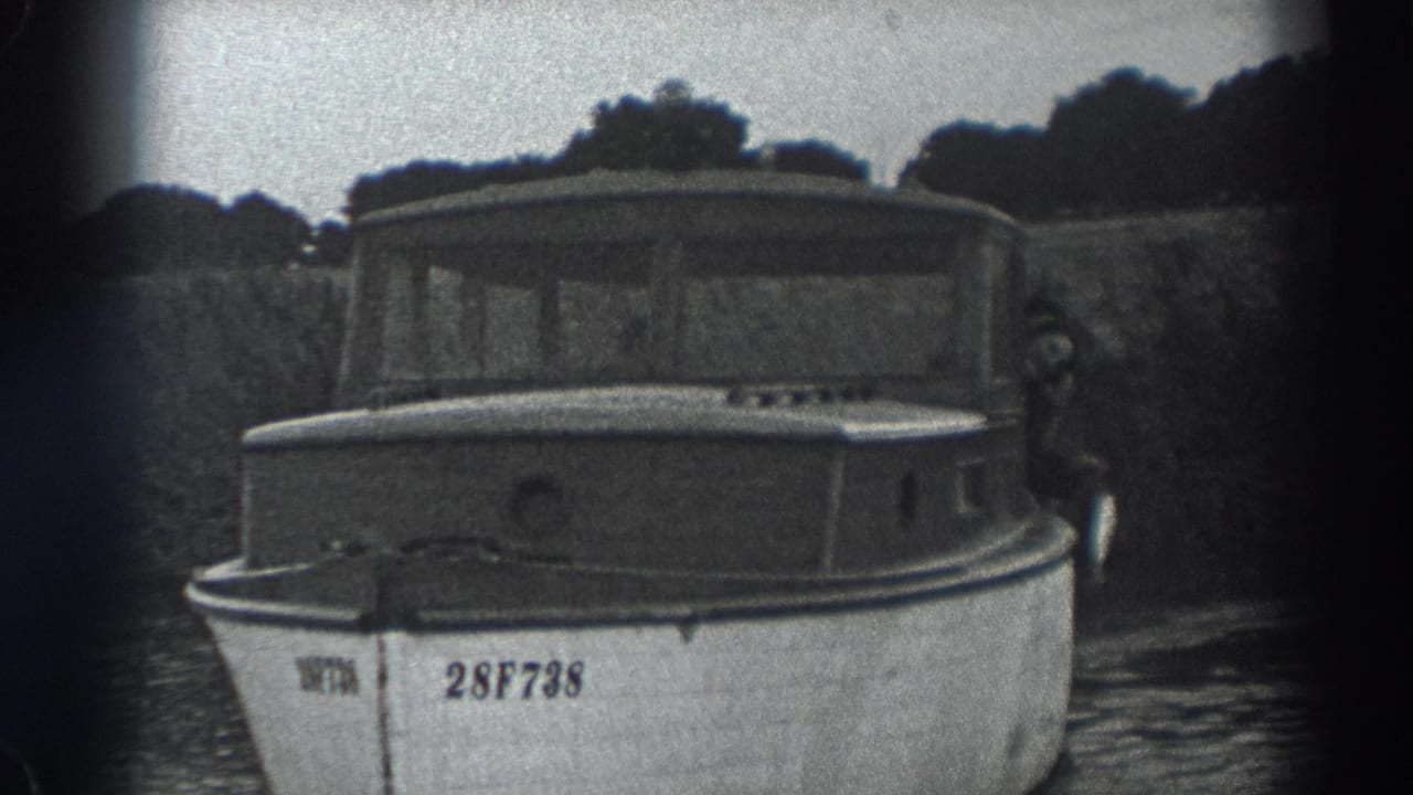 Small cabin motorboat facing the camera on calm water with trees behind it.