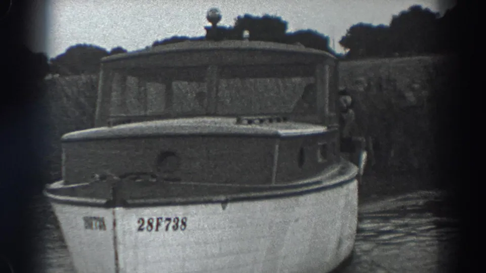 1938 Fort Ross frame of a white cabin motorboat on water, with a person partly visible beside the cabin.