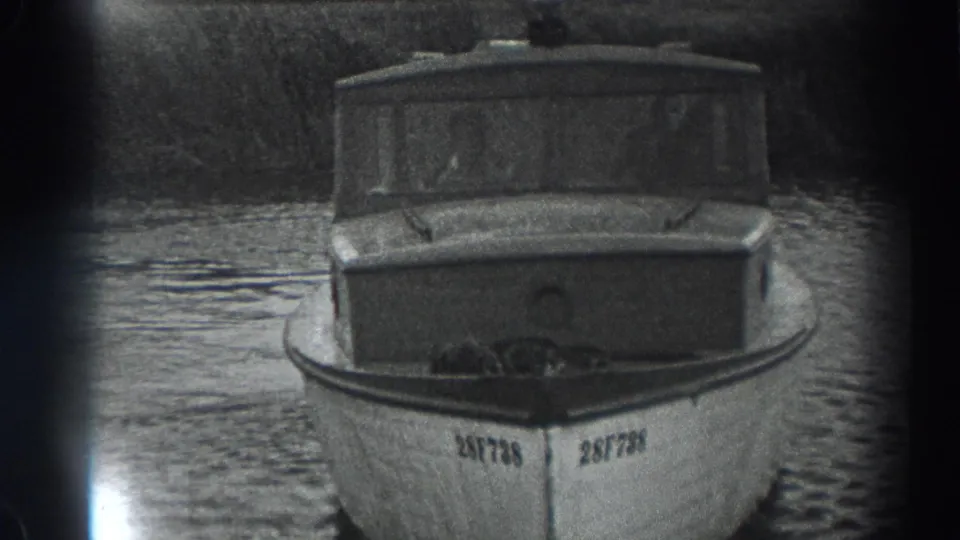 Black-and-white 8mm frame from Fort Ross showing a small registered cabin boat on a calm river.