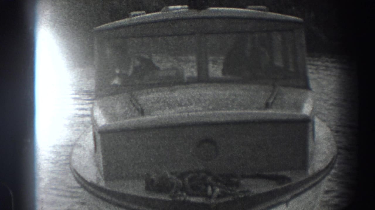 Small cabin motorboat on calm water, seen through a dark rounded 8mm frame edge.
