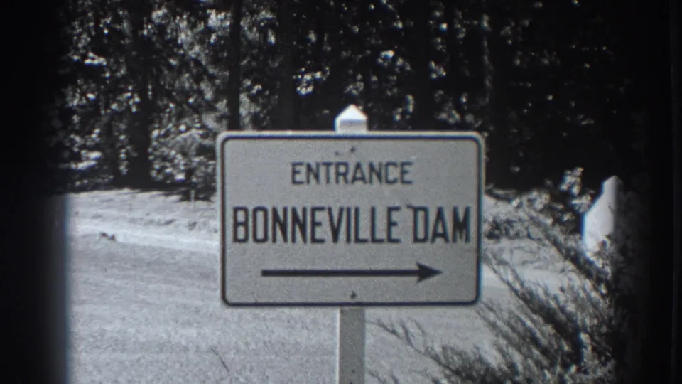 1938 home-movie frame of a roadside Entrance Bonneville Dam sign with a right-pointing arrow near trees.