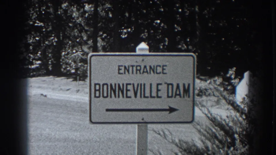 Close 1938 8mm frame of the Entrance Bonneville Dam sign, right arrow, roadside, and wooded backdrop.