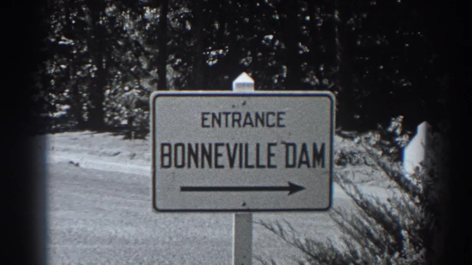 1938 8mm home-movie frame centering the Bonneville Dam entrance sign along a wooded roadside.