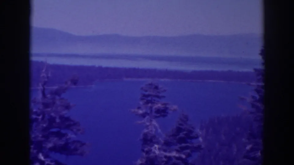 1938 Lake Tahoe scenery with a broad blue lake, conifer shapes in the foreground, and layered mountains under haze.