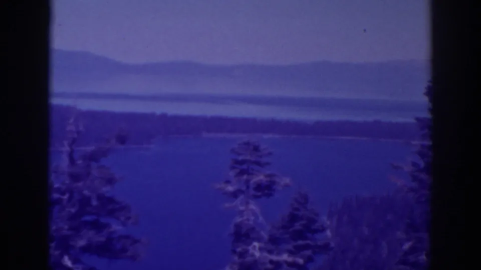 Lake Tahoe landscape on 8mm film, showing a blue water surface, dark trees, wooded shore, and soft mountain horizon.