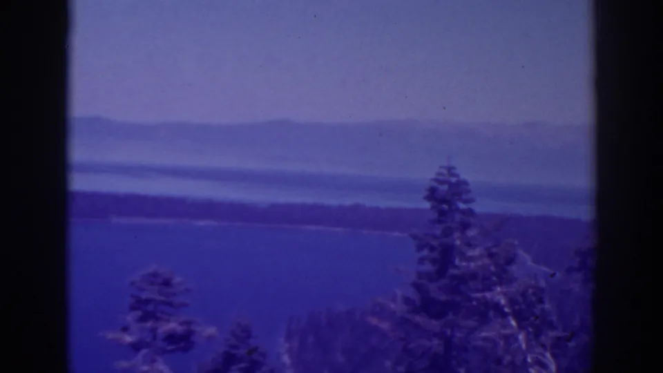 A 1938 home-movie frame looks over evergreen treetops toward Lake Tahoe, a wooded shore, and muted hills in soft focus.