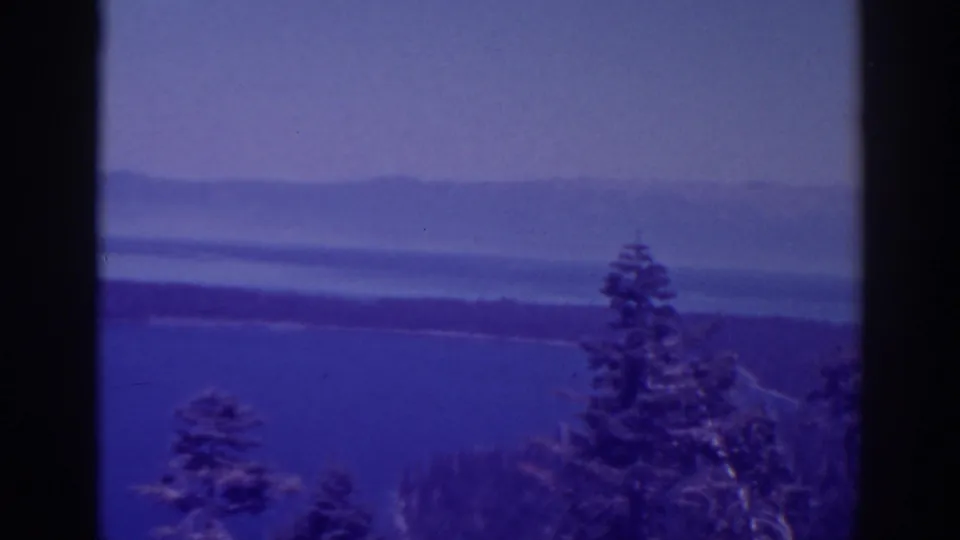 The final frame holds on a Lake Tahoe overlook, with foreground evergreens, open blue water, a far wooded shore, and hazy hills.