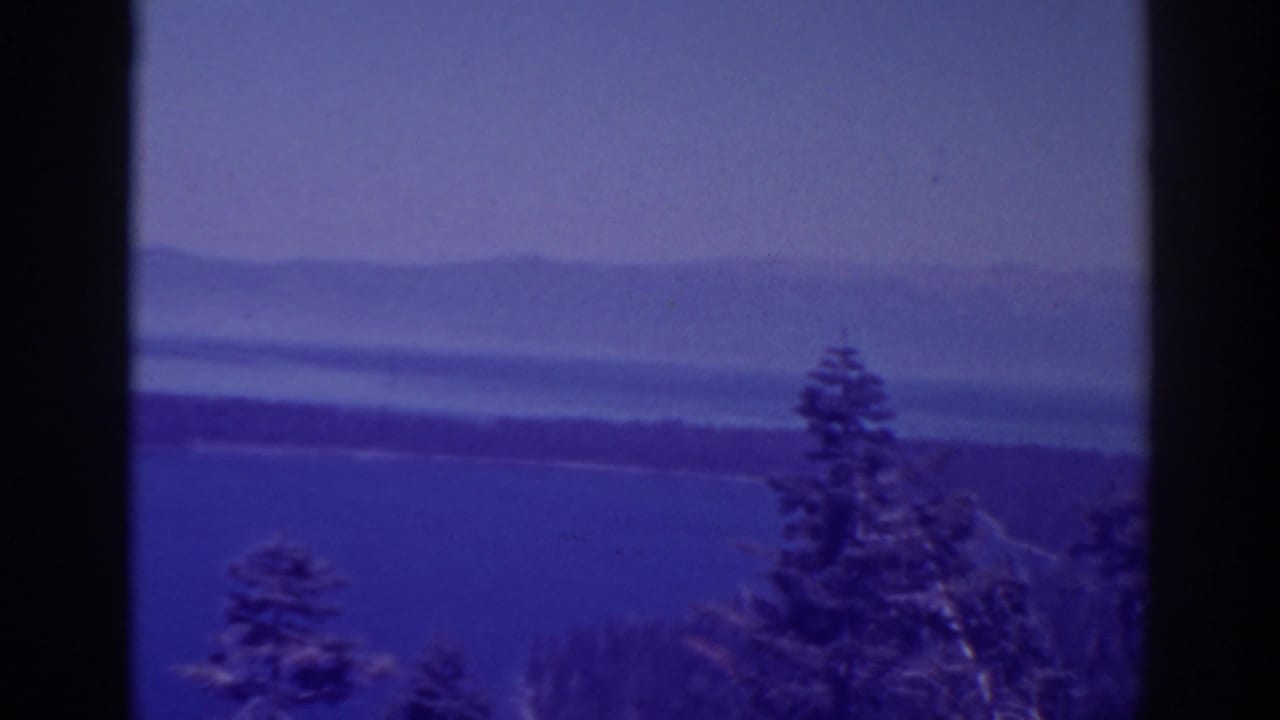 Wide lake view with trees in front and hazy mountains across the water.