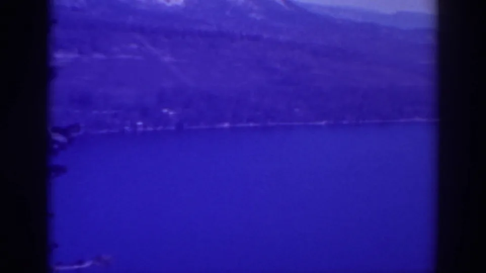 Blue-shifted 1938 Lake Tahoe view with open water, a distant tree-lined shore, and layered mountain slopes.