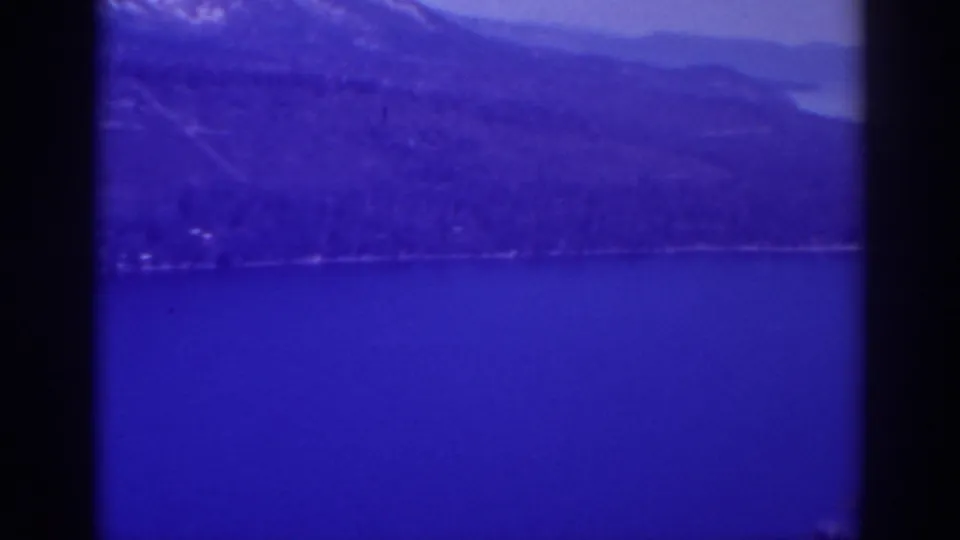 1938 8mm view across Lake Tahoe, with a possible far-shore road or path below forested slopes and mountains.