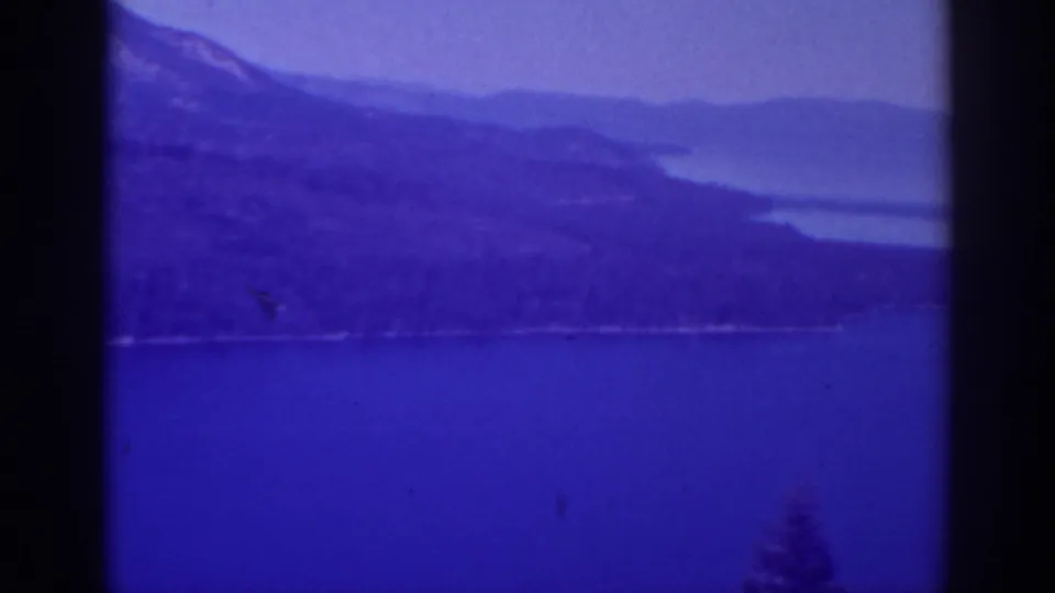 1938 Lake Tahoe home-movie frame showing calm blue water, hazy mountain ridges, and pine-covered shoreline.