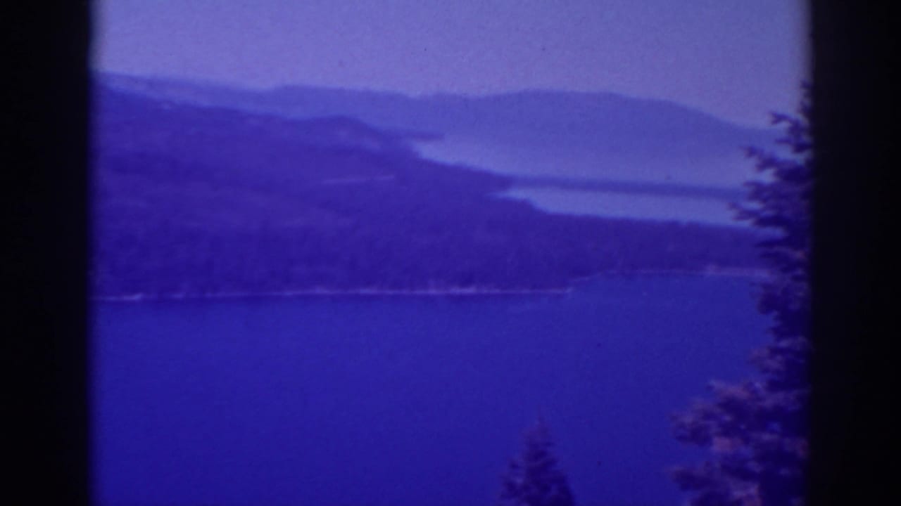 Lake water, mountain ridges, and a dark vertical film border with trees at the right edge.