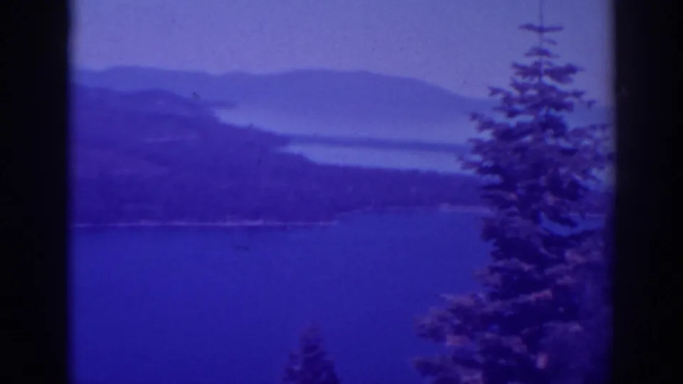 1938 Lake Tahoe home-movie view with foreground pines, blue lake water, and soft distant mountain forms.