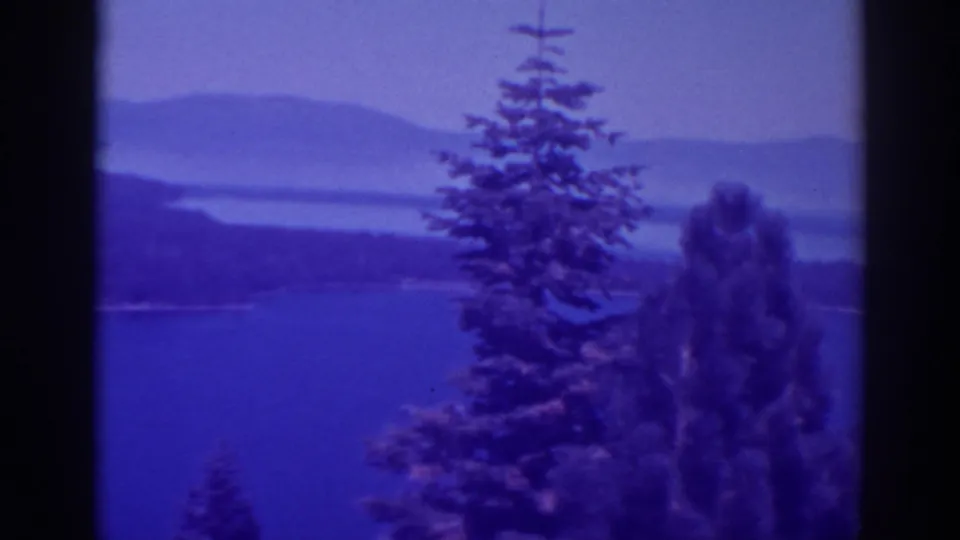 1938 Lake Tahoe home-movie frame showing evergreens above blue lake water and distant hazy hills.
