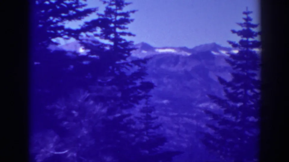 1938 Lake Tahoe home-movie frame with dark pines and distant snow-marked mountain ridges.