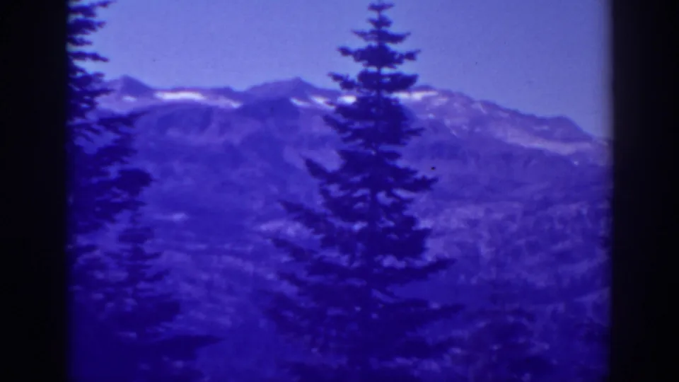 Late-1930s Lake Tahoe mountain view with a central evergreen and blue-purple color shift from 8mm film.
