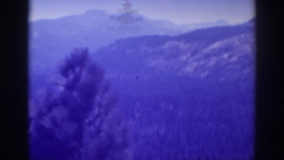 1938 Lake Tahoe frame showing hazy mountain layers, foreground brush, and a soft blue-purple 8mm home-movie color cast.