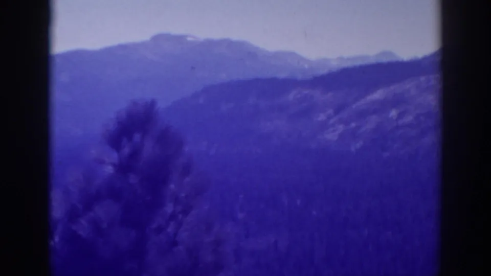 Lake Tahoe winter landscape in 1938 8mm footage, with layered mountain ridges, wooded slopes, and blurred foreground vegetation.