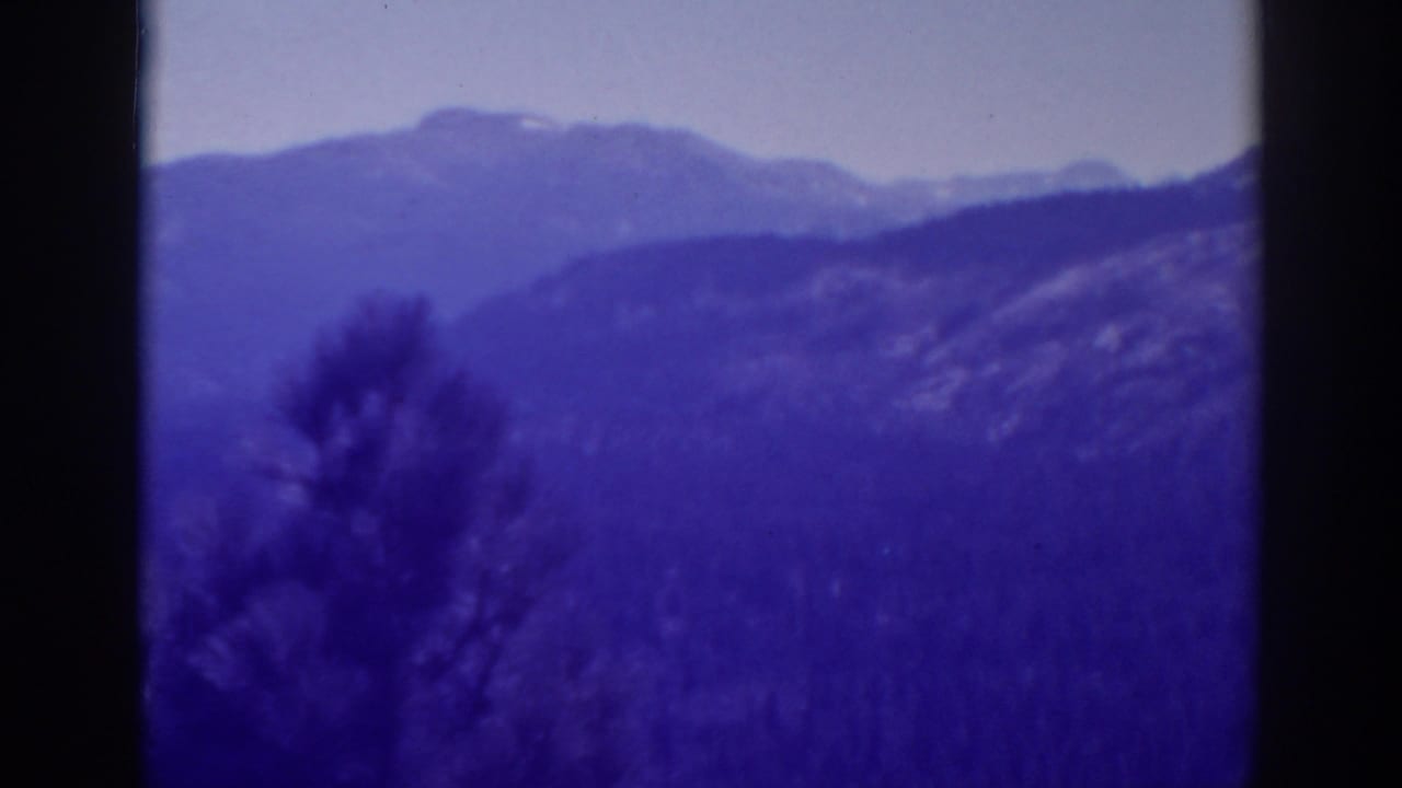 Blue-purple mountain landscape with a dark tree silhouette at left and cloudy sky above.