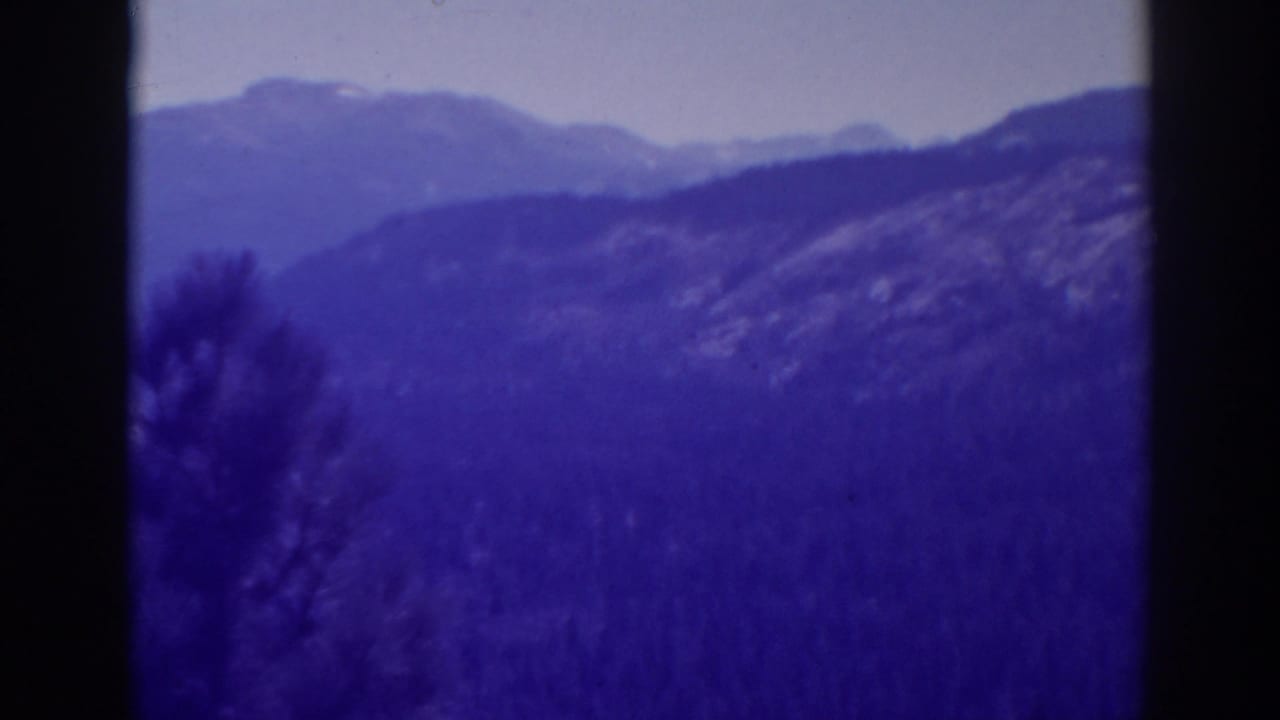 Soft blue mountain ridges with wooded hillsides and dark vertical film borders.