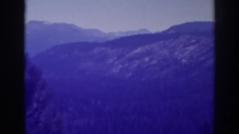 1938 Lake Tahoe 8mm frame showing a misty hillside, distant ridges, cloudy sky, and partial tree silhouette at the edge.