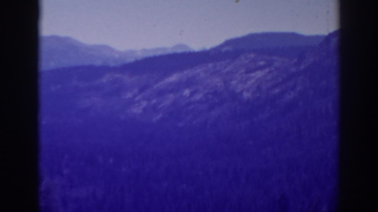 1938 8mm home-movie view of layered High Sierra mountain ridges, likely near Lake Tahoe, with strong purple color aging.
