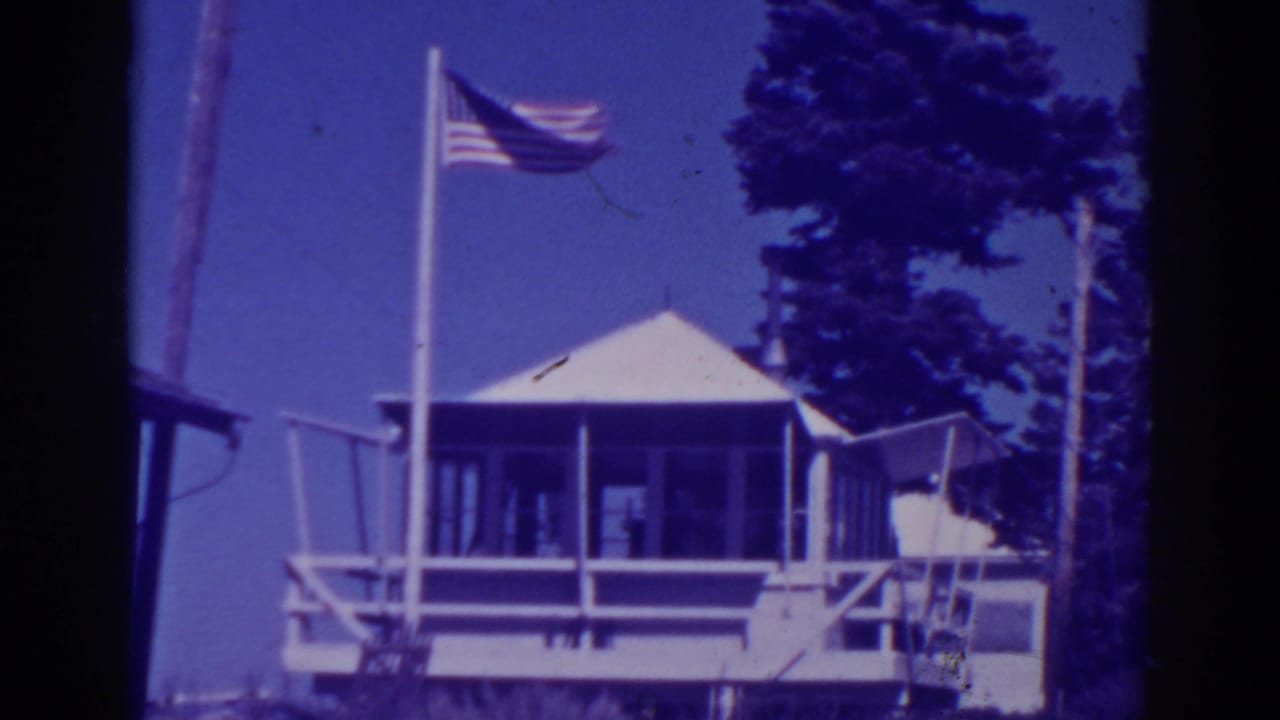 American flag flying beside a small wooden lookout station among pine trees.