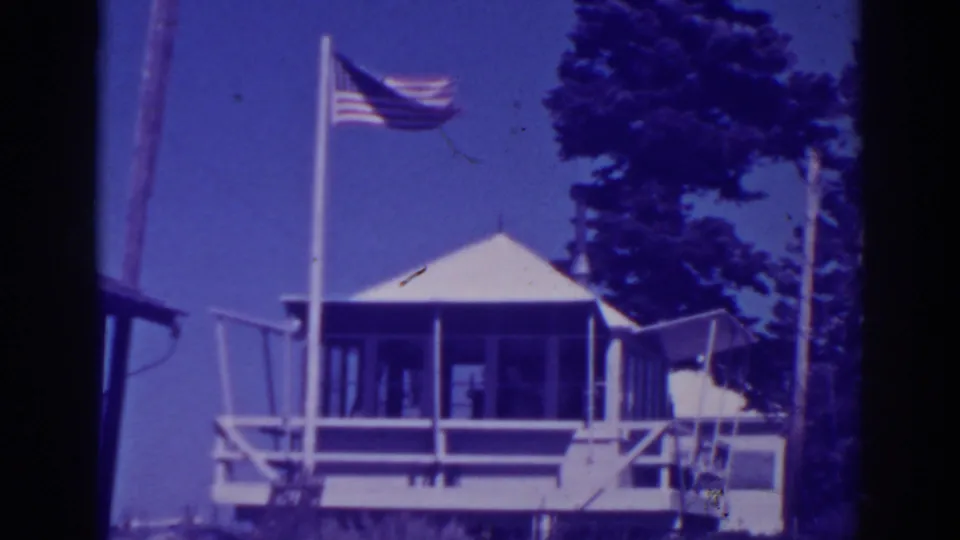 Lake Tahoe-area 1938 8mm view of an American flag and wooden lookout station under a blue sky.