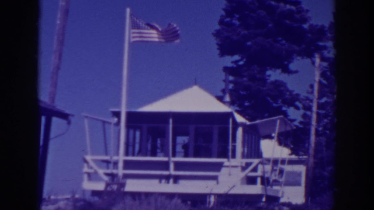 American flag above a white lodge porch with pine trees in the background.