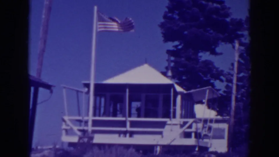 Lake Tahoe lodge exterior in 1938 footage, with the American flag raised above the porch and dark pine trees behind.