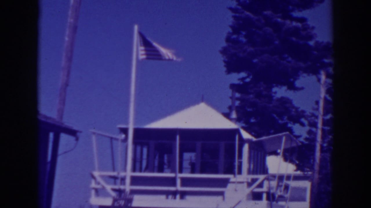 1938 Lake Tahoe home-movie frame showing Martin's Lodge exterior with an American flag flying near pine trees.