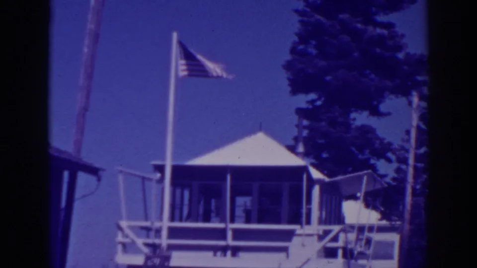1938 Lake Tahoe home-movie frame showing Martin's Lodge exterior with an American flag flying near pine trees.