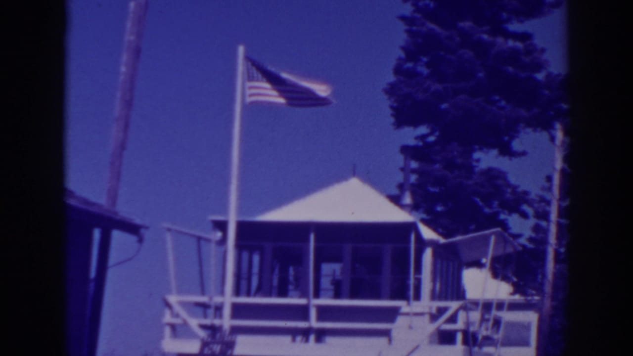 Lodge roof and porch with an American flag waving above trees and sky.