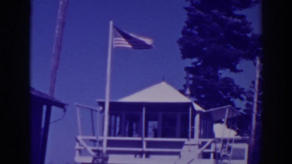 Lake Tahoe lodge exterior in 1938, with a flagpole, American flag, porch structure, and tall pines visible.