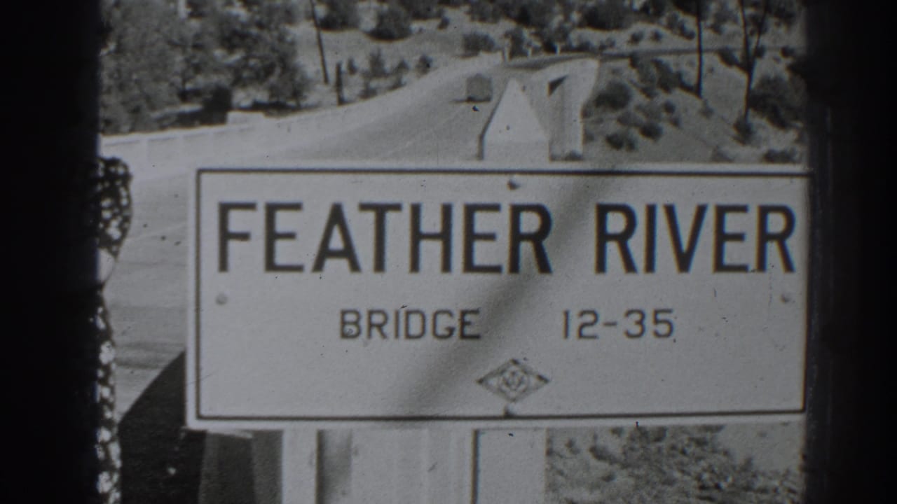 Feather River Bridge sign beside a roadway with trees and hills beyond.